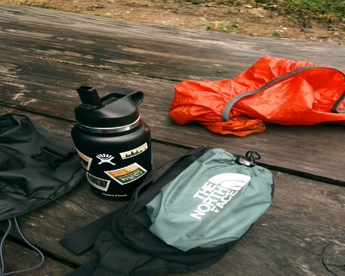 English description: Organized camping gear laid out on a wooden table, including boots, backpack, and a thermos