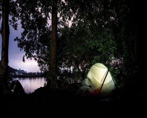 English description: A modest green tent pitched legally at a designated German campsite near a lake